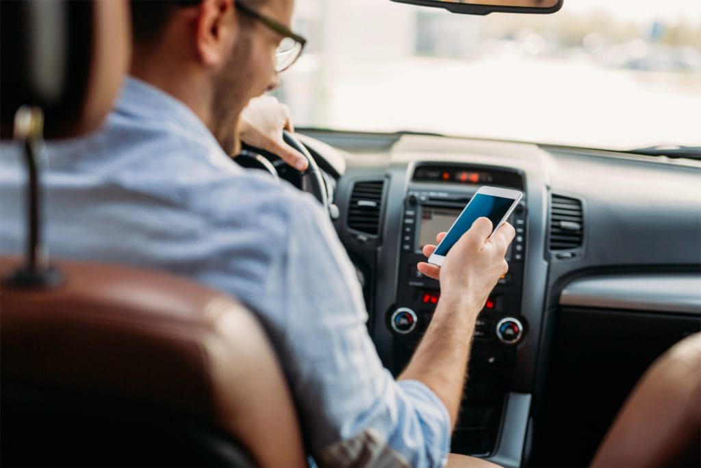 Driver texting on phone while driving in Houston traffic, showing risk of distracted driving