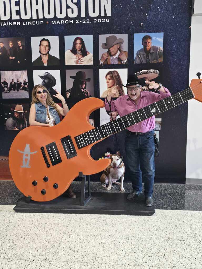 Adam H. Miller, The Texas Bulldog, and Houston's LaLa posing with a giant guitar display and a dog at RodeoHouston 2026