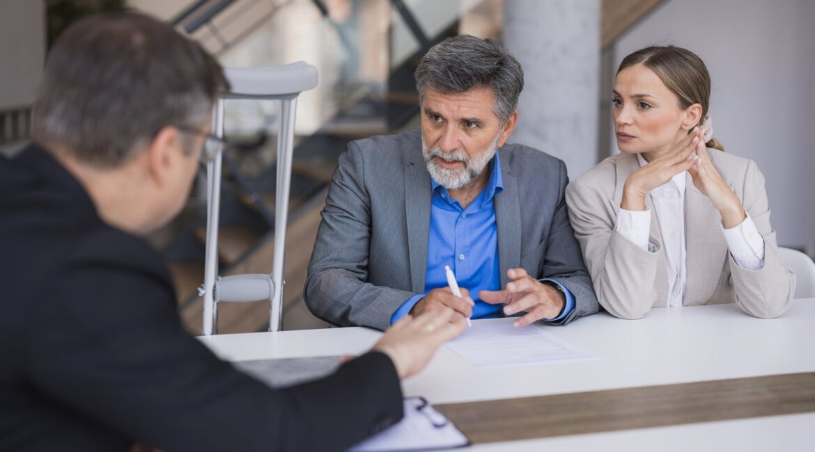 A personal injury attorney consulting with a client on crutches and his wife about their accident claim