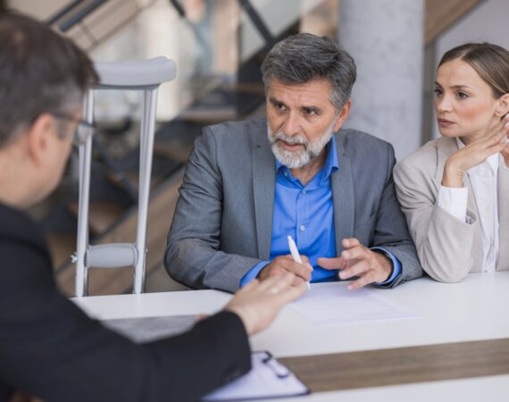 A personal injury attorney consulting with a client on crutches and his wife about their accident claim