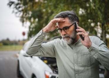 Worried Houston driver with his hand on his forehead calling for help on his phone beside a damaged car after a crash