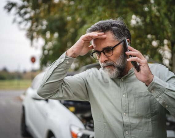 Worried Houston driver with his hand on his forehead calling for help on his phone beside a damaged car after a crash