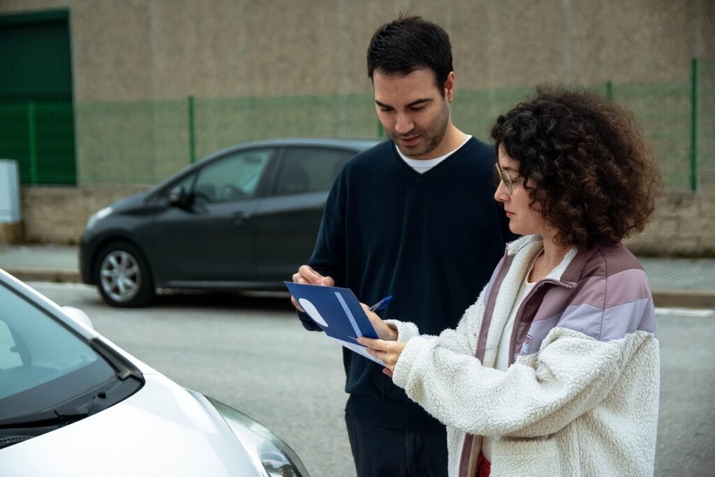 Two drivers checking paperwork together beside their cars after a crash