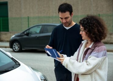 Two drivers checking paperwork together beside their cars after a minor crash, a scene that raises the question of whether Texas is a no-fault state