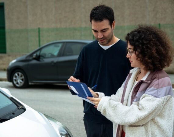 Two drivers checking paperwork together beside their cars after a minor crash, a scene that raises the question of whether Texas is a no-fault state